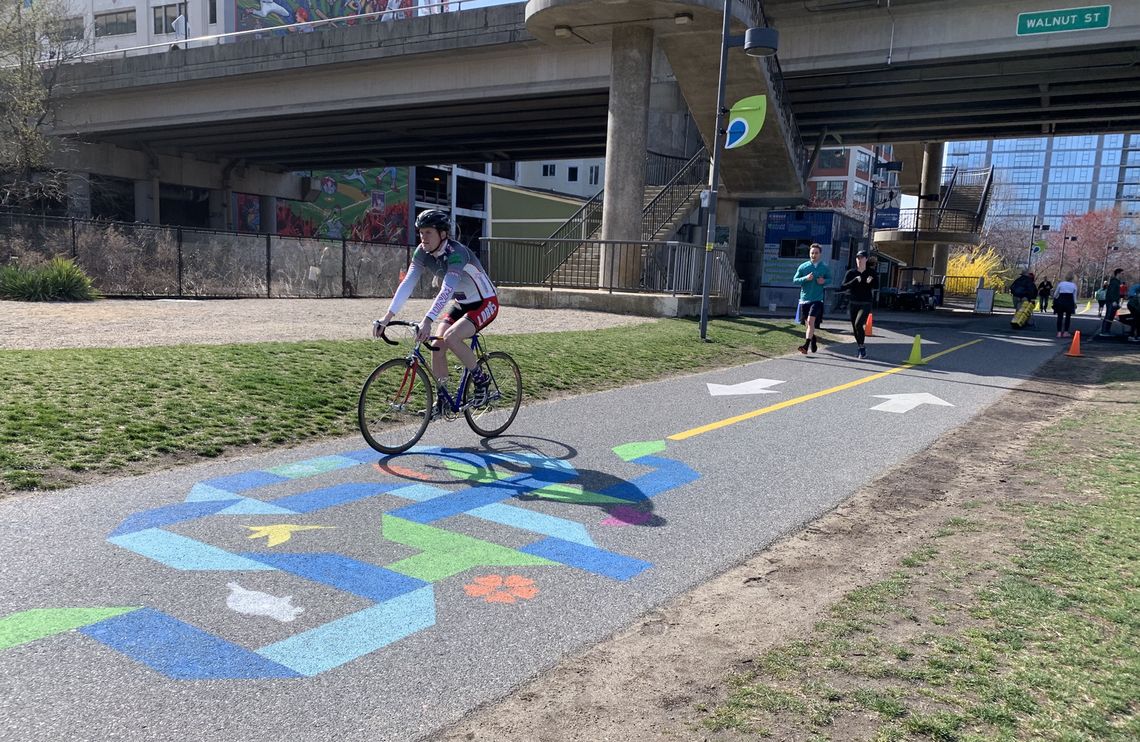 Cyclists and runners pass a chalk-art mural that artist William Woodsey created for the East Coast Greenway along the Schuylkill Banks trail in time for the Summit. The art, including the Greenway's logo, is also visible from above on the Walnut Street bridge.